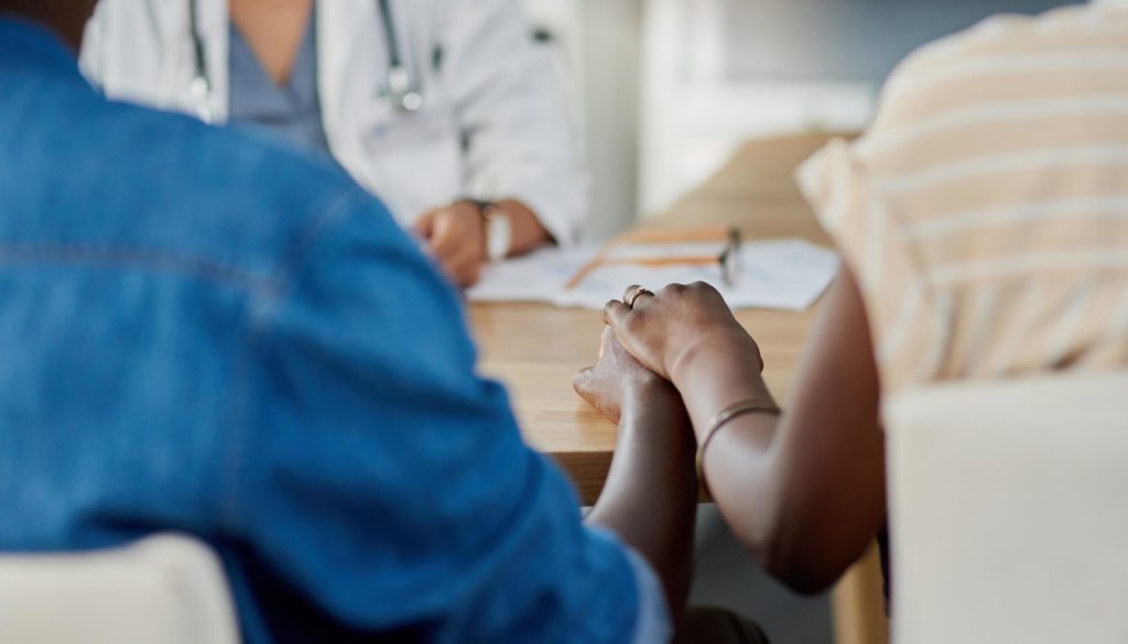 Image of two people holding hands on a desk while at a doctor’s appointment
