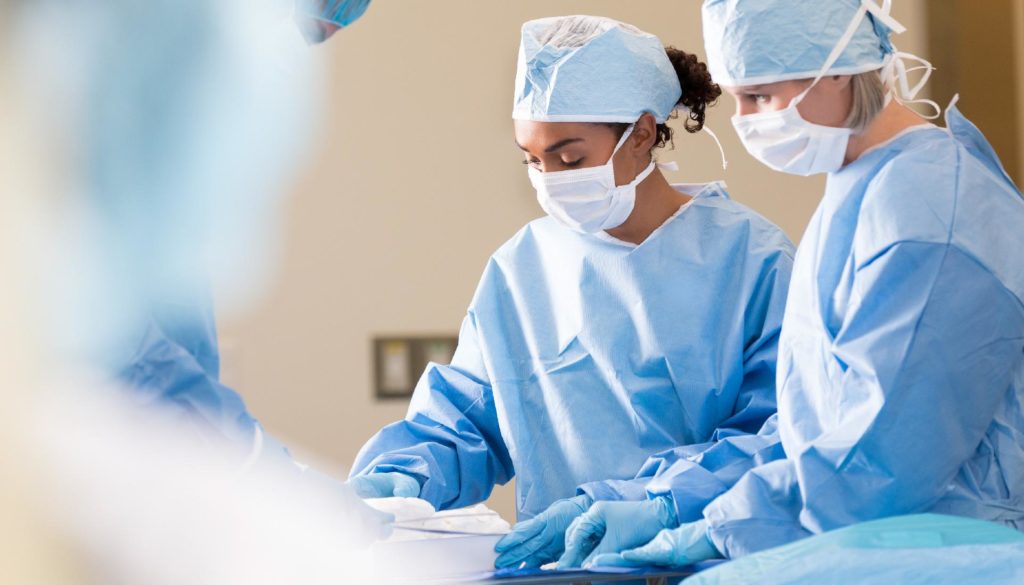 Image of three people in surgical scrubs looking down and performing a surgery or procedure