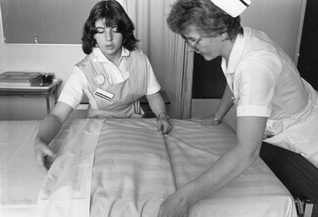 A young nurse and her supervisor adjust a bedsheet