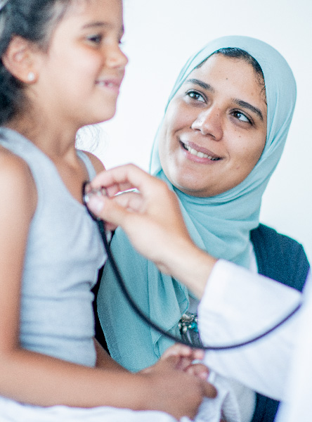 doctor pressing a stethoscope to the chest of a child while her mother stands by and smiles