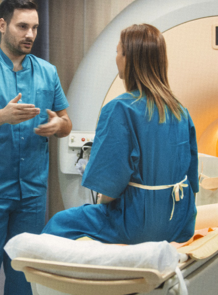 a male doctor stands and talks to a female patient sitting on an mri machine's bed