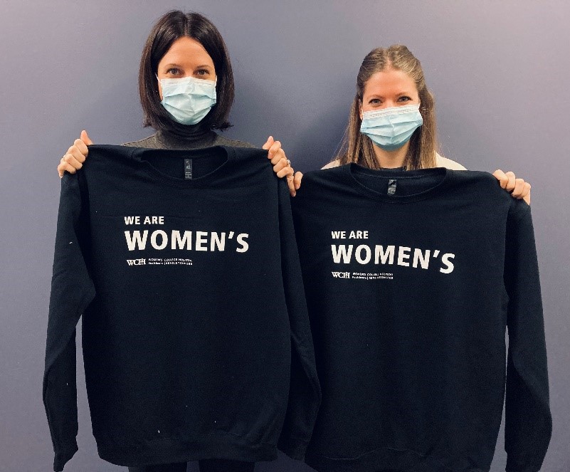 Two women holding up sweatshirts